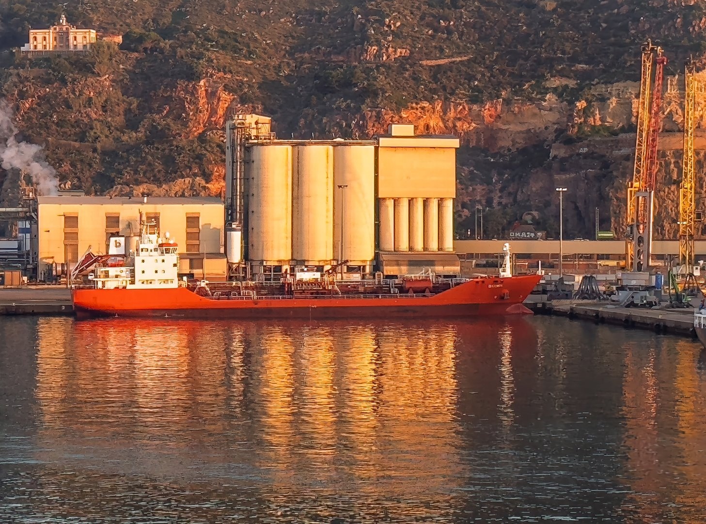 Barcelona, Spain - July 11, 2024: Sunrise over Bunge Iberica tanks and silos on Coma I Ribas Port Terminal. Docked red bunker boat.
